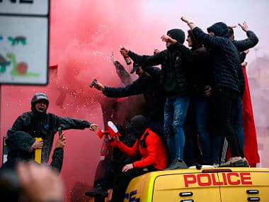 FILE - In this April 24, 2018 file photo, soccer fans stand on top of a police van amid smoke from flares outside the stadium before the Champions League semifinal, first leg, soccer match between Liverpool and AS Roma at Anfield Stadium, Liverpool, England. Roma’s outspoken American president Jim Pallotta has called on Italian supporters to unite in protest following the latest incidents of fan violence involving his club. (AP Photo/Dave Thompson)