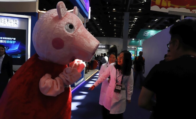 In this April 27, 2018 photo, a woman reacts to a Peppa Pig mascot during the Global Mobile Internet Conference (GMIC) in Beijing, China. The cherubic British cartoon character, Peppa Pig, has become an unlikely target of China's censors as online fans use her porcine likeness in sardonic memes and 