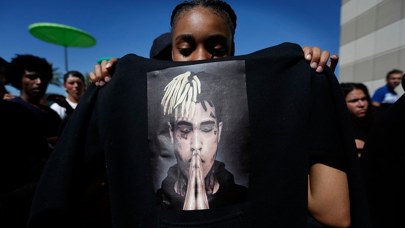 Anneyah Lawson, 14, of St. Petersburg, Fla., holds up a sweatshirt with an image of slain rapper XXXTentacion, before his memorial on 27 June in Sunrise, Fla. Associated Press/Brynn Anderson