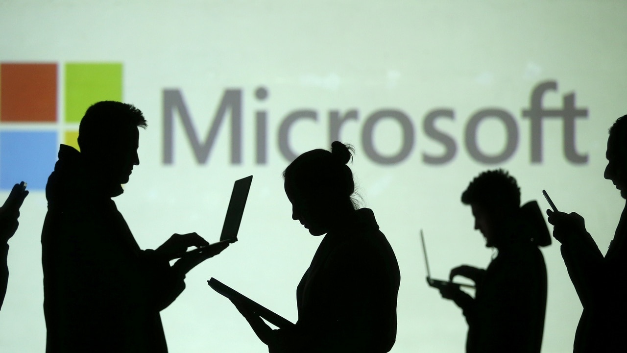 Silhouettes of laptop and mobile device users are seen next to a screen projection of Microsoft logo in this picture illustration taken March 28, 2018.  REUTERS/Dado Ruvic/Illustration - RC1B82FF5300