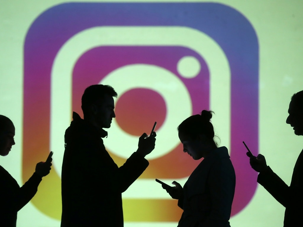 Silhouettes of mobile users are seen next to a screen projection of Instagram. Reuters