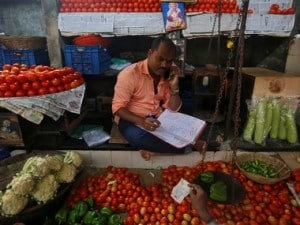 A vendor speaks on his mobile phone as he maintains his ledger book at a stall selling vegetables in Mumbai. Reuters