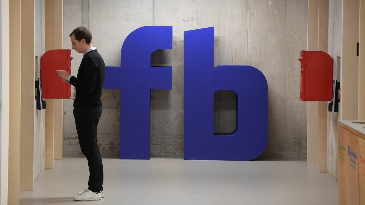 A man waits for an elevator in front of a Facebook logo. Image: Reuters