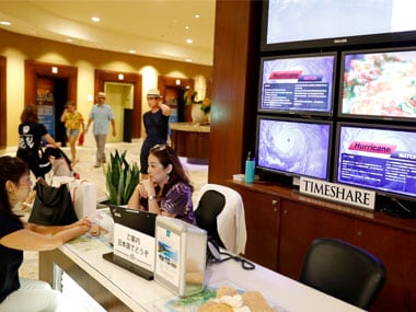 With several monitor displaying hurricane information in several different languages behind them, two women sit at a desk inside a Waikiki hotel in Honolulu. AP