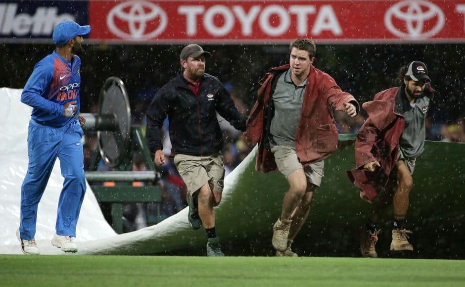 Players leave the field as ground staff cover the pitch after rain stopped play during the first T20 International cricket match between Australia and India in Brisbane, Australia, Wednesday, Nov. 21, 2018. (AP Photo/Tertius Pickard)