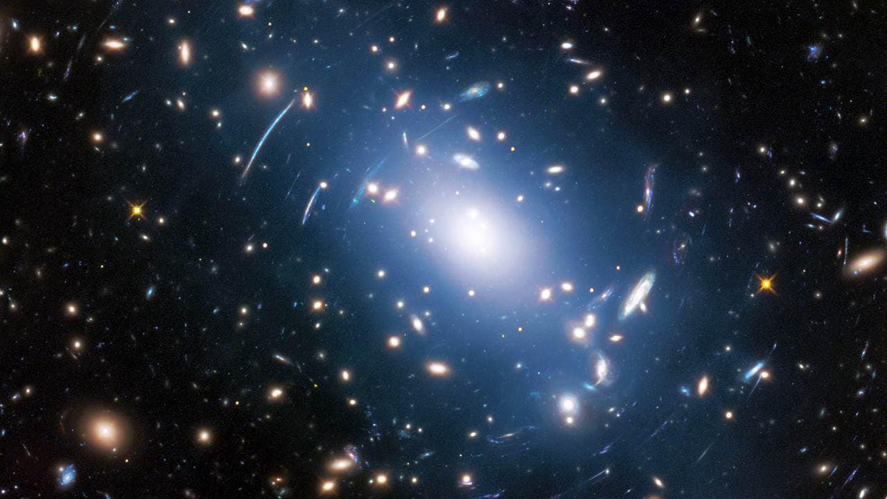 Abell S1063, a galaxy cluster, was observed by the NASA/ESA Hubble Space Telescope as part of the Frontier Fields programme. The huge mass of the cluster — containing both baryonic matter and dark matter — acts as cosmic magnification glass and deforms objects behind it. In the past astronomers used this gravitational lensing effect to calculate the distribution of dark matter in galaxy clusters. A more accurate and faster way, however, is to study the intracluster light (visible in blue), which follows the distribution of dark matter. Image: ESA