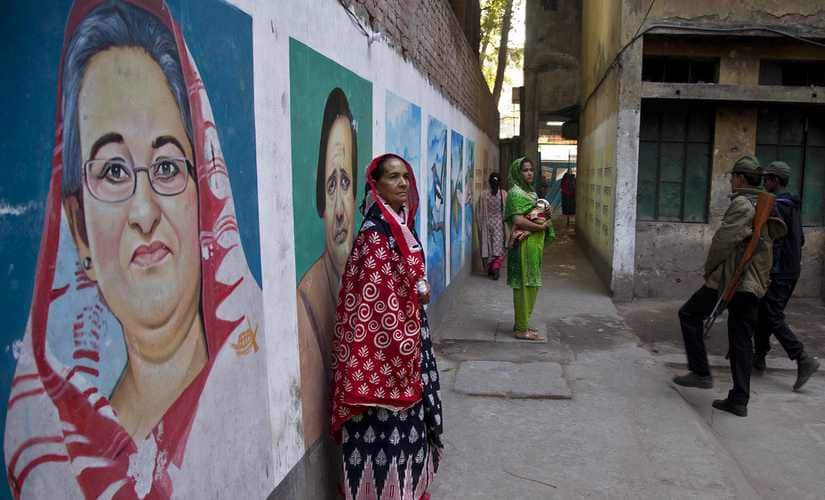 Bangladeshi women stand next to a mural displaying portraits of Bangladesh Prime Minister Sheikh Hasina. AP