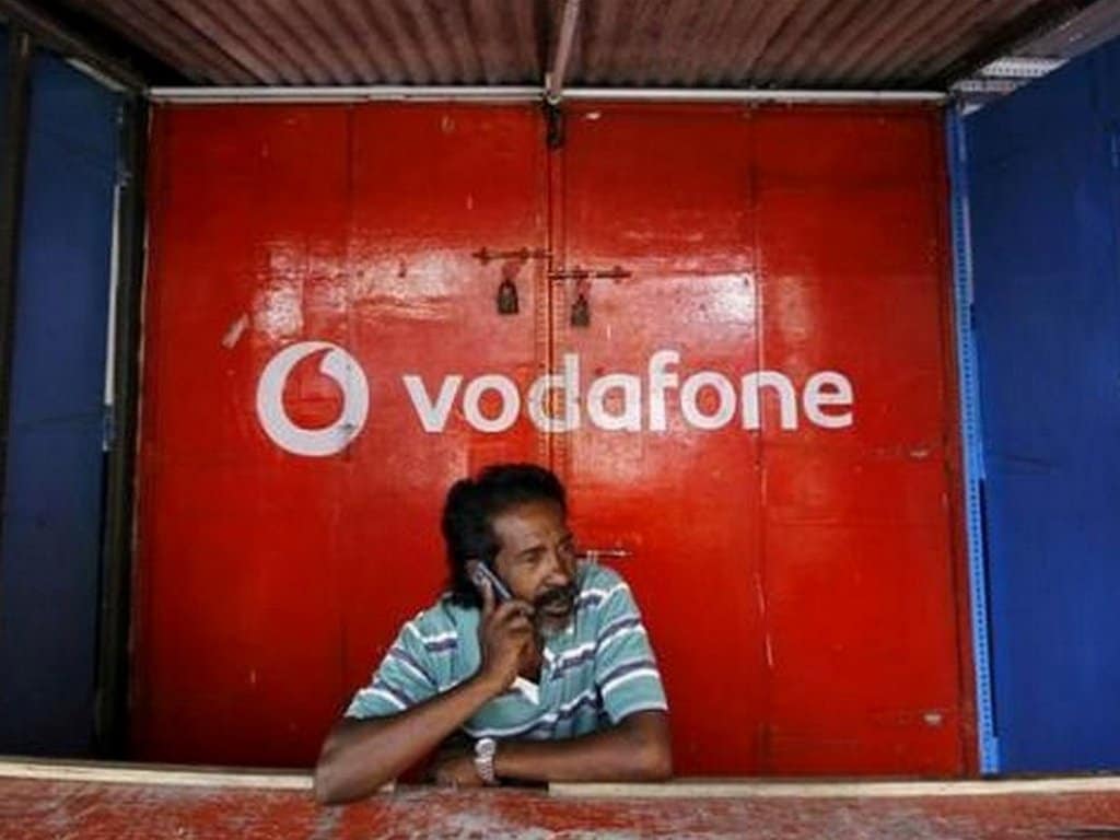 FILE PHOTO: A retail shop owner speaks on his mobile phone outside his closed shop shutters painted with an advertisement for Vodafone at a market in Chennai
