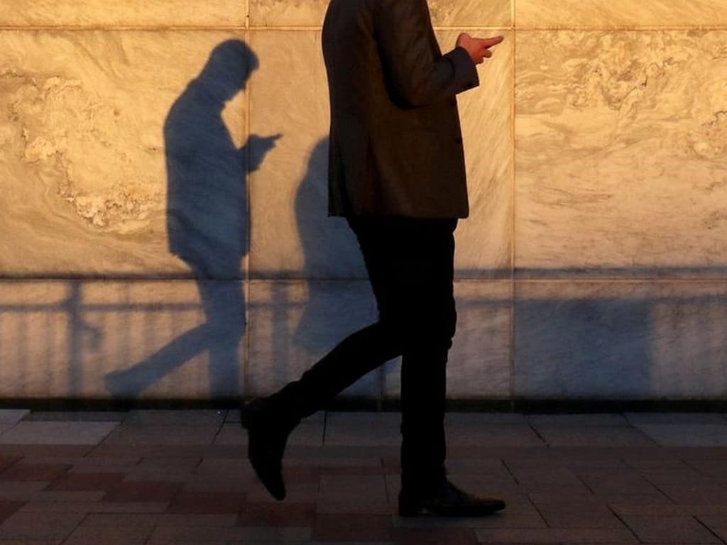 FILE PHOTO: An unidentified man using a smart phone walks through London's Canary Wharf financial district in the evening light in London, Britain, September 28, 2018. REUTERS/Russell Boyce/File Photo