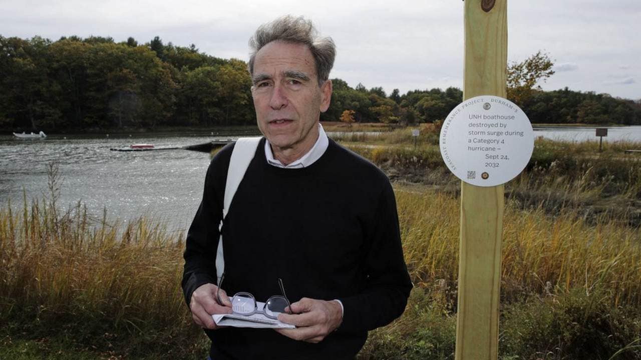 Artist Thomas Starr poses next to a sign, part of a public design installation, on the banks of the Oyster River in Durham, N.H. Image credit: AP