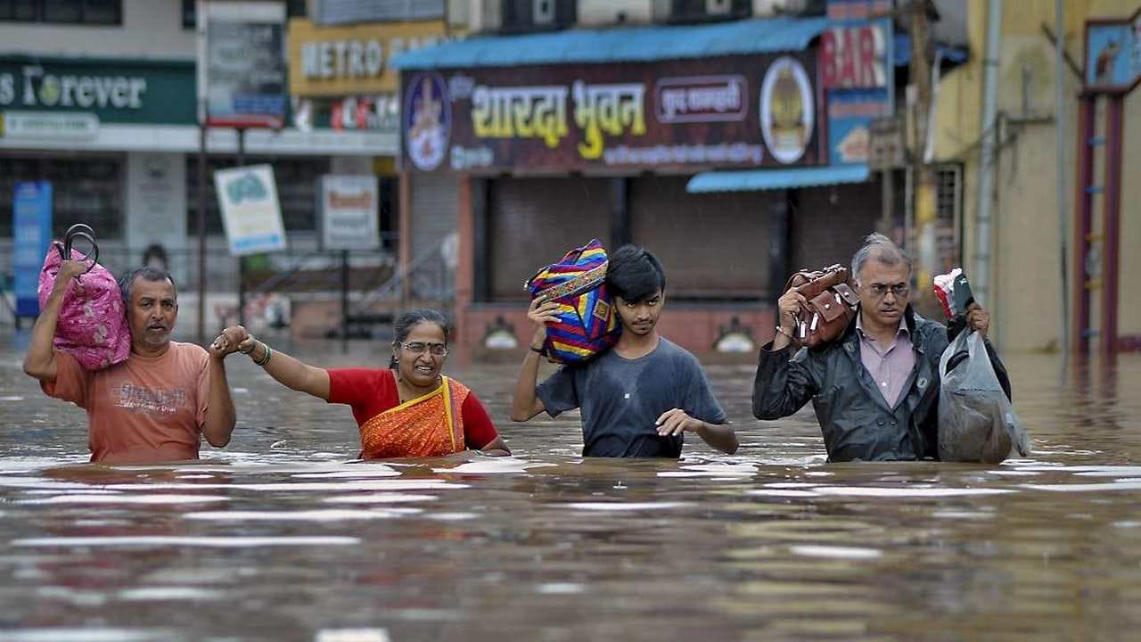 Sangli: Residents wade across a flooded street with their belongings to relocate to a safer place due to overflowing Krishna river during monsoon season, in Sangli, Wednesday, Aug 7, 2019. (PTI Photo) 