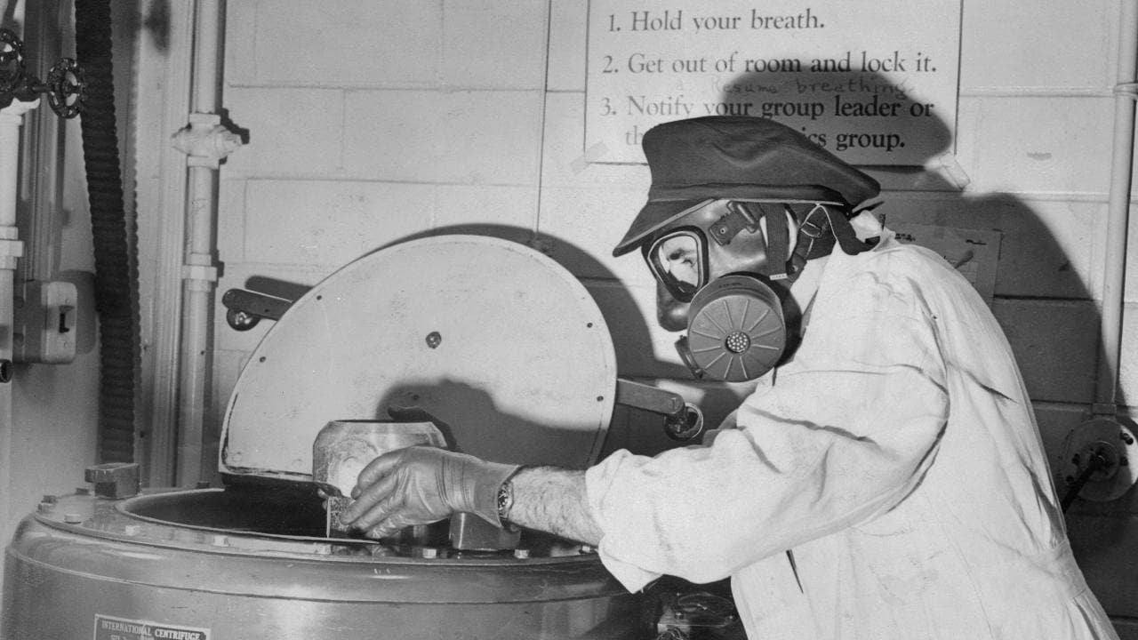 Man in Uniform Working with Radioactivity (Original Caption) Jacob Sedlet, a laboratory chemist wearing mask and gloves, here takes radioactive material from centrifuge at University of Chicago.