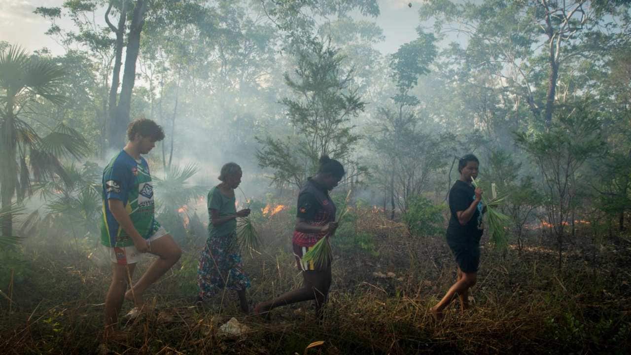 Violet Lawson (second from left) and others in her family chew on green sand palm fronds for hydration while out burning brush near Cooinda in Northern Australia, on 15 January 2020. Image: Matthew Abbott/NYT
