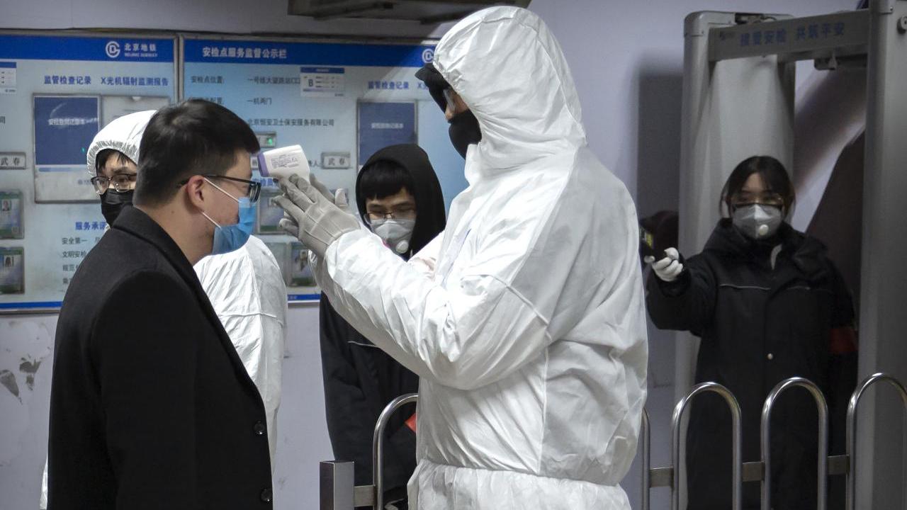 A worker wearing a hazardous materials suit takes the temperature of a passenger at the entrance to a subway station in Beijing, Image credit: AP