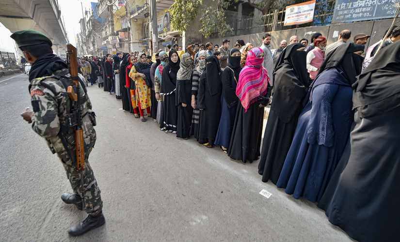Asecurity personnel stands guard as voters stand in a queue to cast vote during the Delhi Assembly elections at a polling station, in Jafrabad area of Delhi. PTI