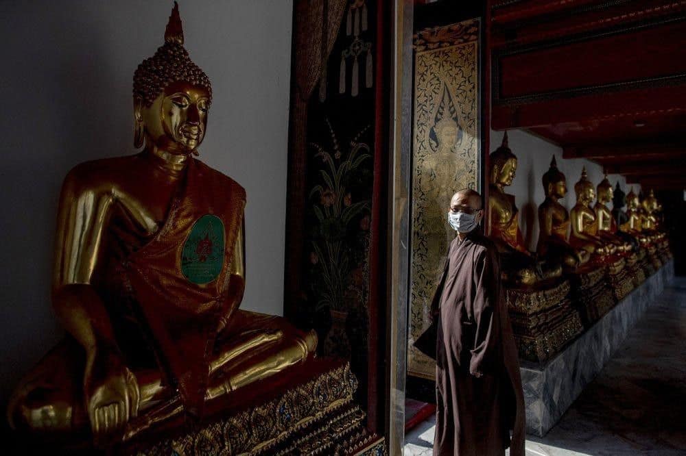 a Buddhist monk from Vietnam wearing a face mask walks amid Buddhist statues at Wat Pho in Bangkok, Thailand. Image credit: AP