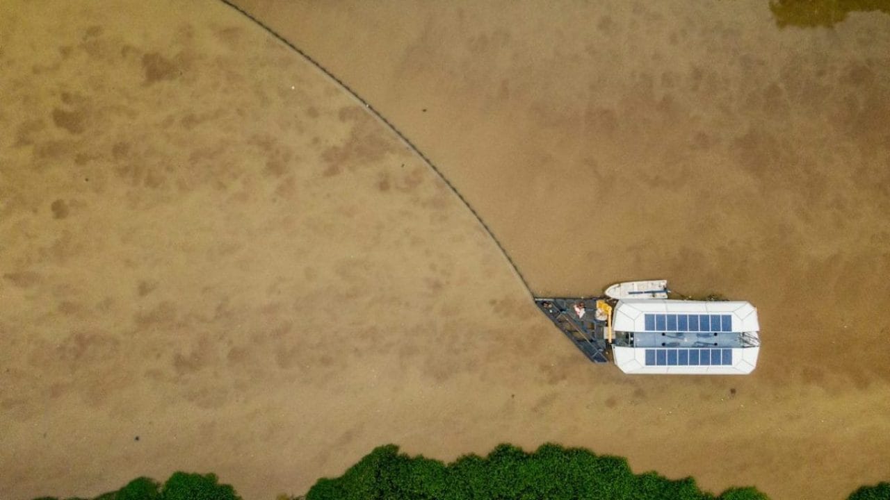 Aerial view of the prototype of the Interceptor, which was installed in Cengkareng drain in Jakarta, Indonesia, in May 2019. A long barrier guides trash toward the device’s mouth. Image courtesy of The Ocean Cleanup.