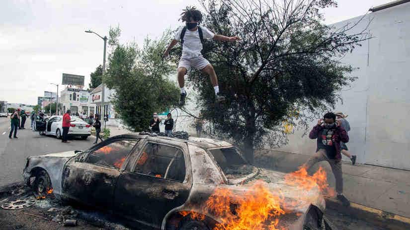 A person jumps on a burning police vehicle in Los Angeles, Saturday, May 30, 2020, during a protest over the death of George Floyd. Floyd died in Minneapolis police custody on Memorial Day. AP Photo/Ringo HW Chiu