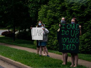 Protesters hold up signs as President Donald Trump’s motorcade passes en route the Trump National Golf Club in Sterling, Virginia. By Anna Moneymaker © 2020 The New York Times 