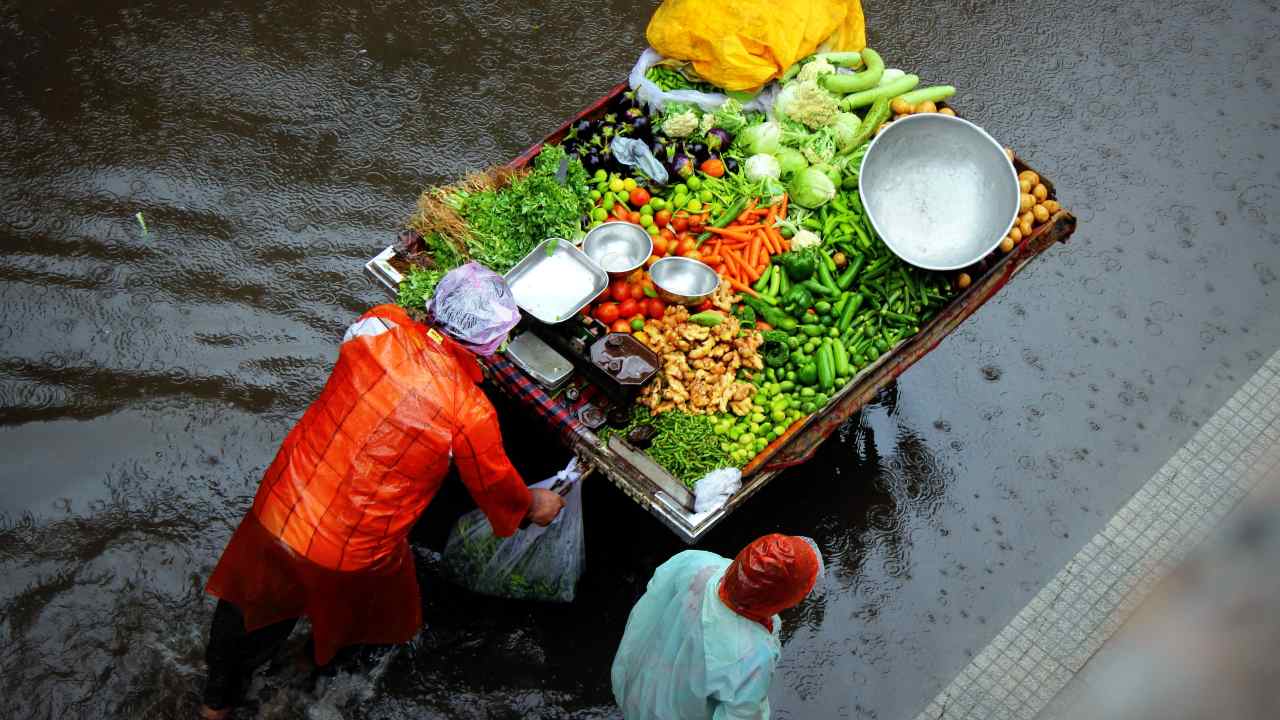 A vegetable vendor pushes his cart through a flooded street. 