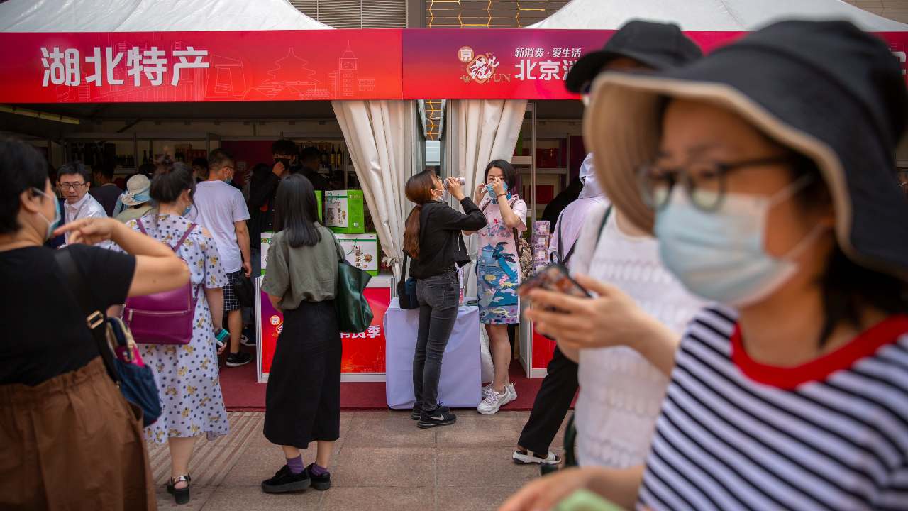 people wearing face masks to protect against the new coronavirus browse merchant tents at a government event aiming to stimulate consumer demand and consumption in Beijing. (AP Photo/Mark Schiefelbein)