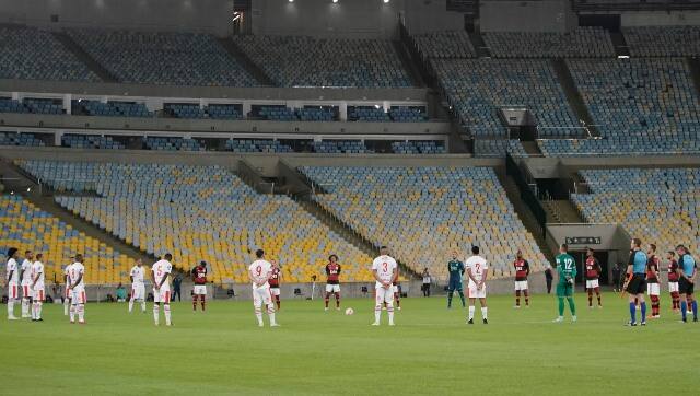 Players of Bangu, wearing white uniforms, and Flamengo pay a minute of silence for the victims of the coronavirus prior to a Rio de Janeiro soccer league match at the Maracana stadium in Rio de Janeiro, Brazi, Thursday, June 18, 2020. Rio de Janeiro’s soccer league resumed after a three-month hiatus because of the coronavirus pandemic. The match is being played without spectators to curb the spread of COVID-19. (AP Photo/Leo Correa)