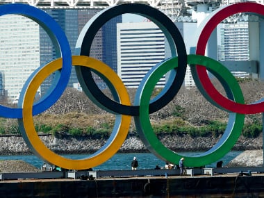 Workers stand at the bottom of the Olympic rings at Tokyo's Odaiba district Tuesday, March 24, 2020, in Tokyo. The Tokyo Olympics are probably going to happen, but almost surely in 2021 rather than in four months as planned. (AP Photo/Eugene Hoshiko)