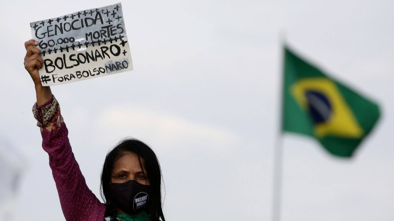 An activist holds a sign that reads ‘Genocide 60,000 deaths, Bolsonaro out,’ in Portuguese, during a protest against the government’s inefficiency in tackling the coronavirus pandemic, alongside with police brutality against blacks, in Brazil, on 2 July. Image: AP