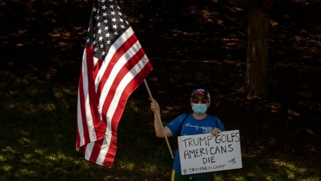 A protester holds the US flag and a sign as President Donald Trump’s motorcade leaves the Trump National Golf Club in Sterling, Virgina, en route to the White House. Samuel Corum/The New York Times