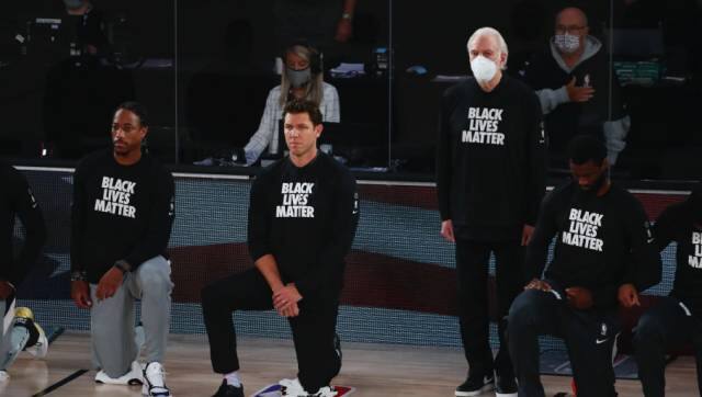 San Antonio Spurs head coach Gregg Popovich, fourth from left, stands while wearing a mask while Sacramento Kings head coach Luke Walton, center, kneels with players before an NBA basketball game Friday, July 31, 2020, in Lake Buena Vista, Fla. (Kim Klement/Pool Photo via AP)