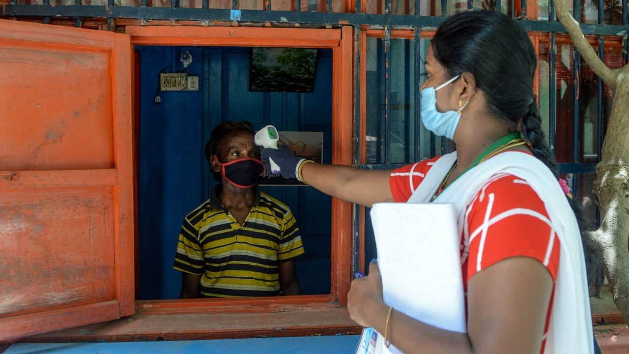Health worker checks the body temperature of a man in Chennai. In April, a 16,000-person surveillance team, mostly women, went door-to-door with minimal personal protective equipment to find people infected with Covid-19. Image credit: Arun Sankar/AFP