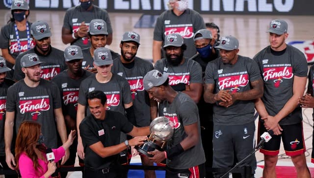 Miami Heat head coach Erik Spoelstra, center left, hands the Eastern Conference trophy to Bam Adebayo (13) as they celebrate their NBA conference final playoff basketball game win over the Boston Celtics with the Eastern Final trophy. Image credit: AP