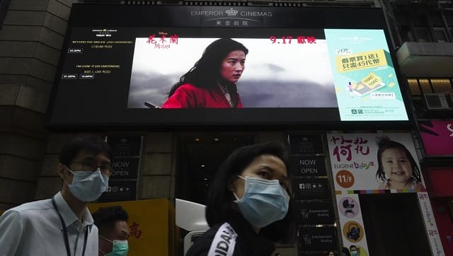 People walk past a huge TV screen showing movie 