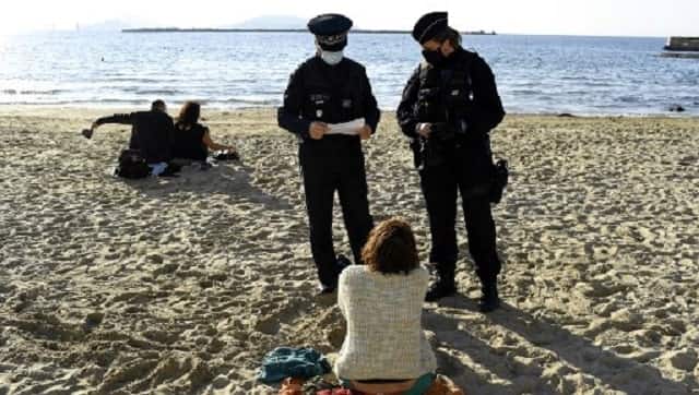French police officials check the written statement of a woman declaring her reason to be out on the beach during lockdown. AFP