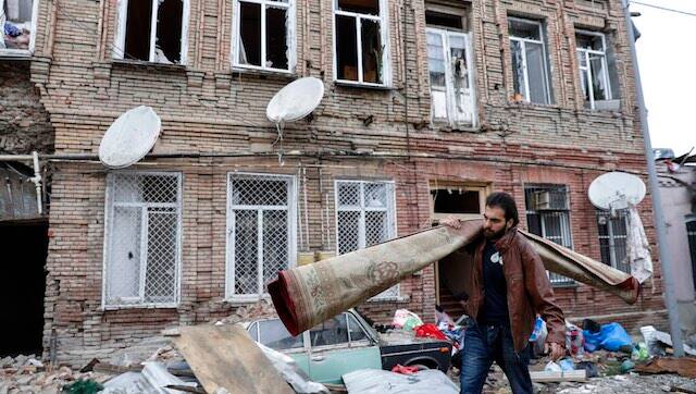 A person carries a carpet as he walks past buildings in a residential area in Ganja, Azerbaijan, damaged by shelling by Armenian forces, 5 October, 2020. AP