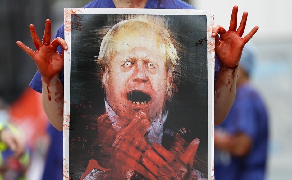 A nurse holds a painting of Prime Minister Boris Johnson clapping with blood on his hands as part of a demonstration of NHS workers at hospitals across London to demand a 15 percent raise. Photo via AP/Kirsty Wigglesworth