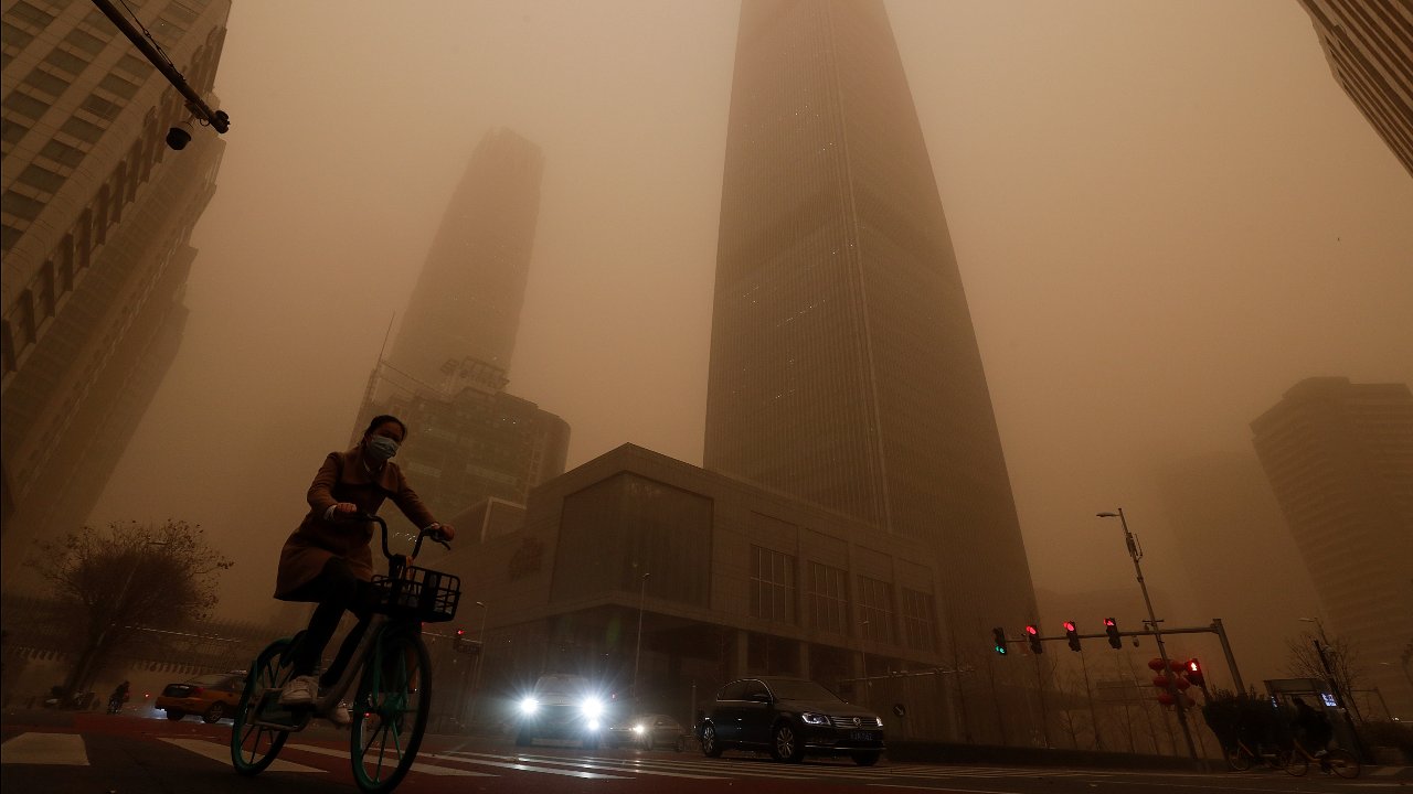 A cyclist and motorists move past office buildings amid a sandstorm during the morning rush hour in the central business district in Beijing, Monday, March 15, 2021. The sandstorm brought a tinted haze to Beijing's skies and sent air quality indices soaring on Monday. Image credit: AP Photo/Andy Wong