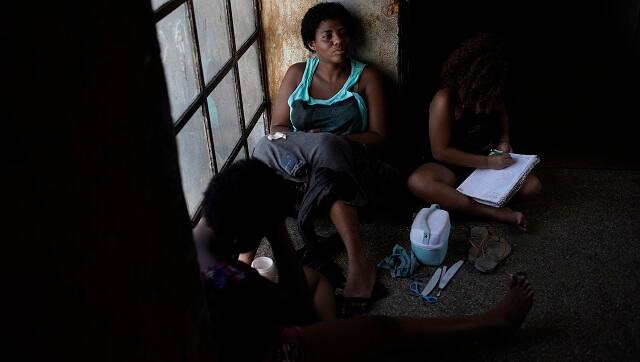 A mother sits on a window seat as she accompanies her daughter inside an occupied building where they live, in Rio de Janeiro. (AP Photo/Silvia Izquierdo)