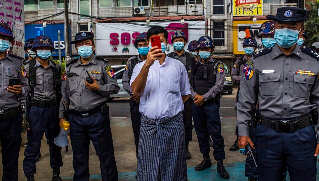 A plainclothes police officer takes a photo of journalists and protesters in Yangon. © 2021 The New York Times