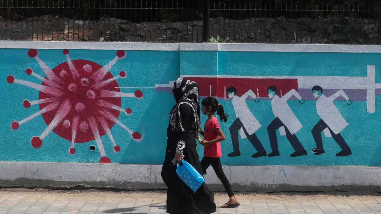 A woman along with a girl walk past a graffiti, depicting the coronavirus in Mumbai, India. Image credit: AP Photo/Rafiq Maqbool