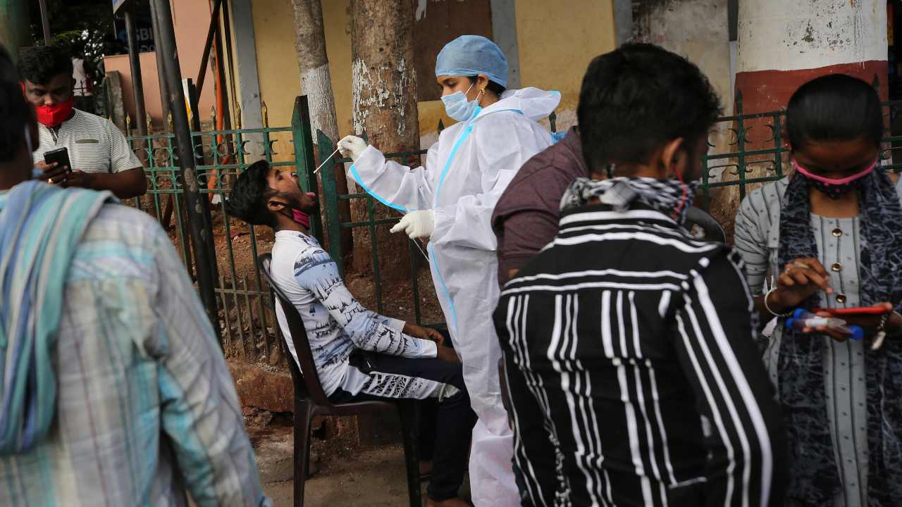 A health worker in protective suit collects mouth swab of a traveler to test for COVID-19 outside a train station in Bengaluru, India, Sunday, April 11, 2021. India is reporting a surge in infections, which according to experts is due in part to growing disregard for social distancing and mask-wearing in public spaces. (AP Photo/Aijaz Rahi)