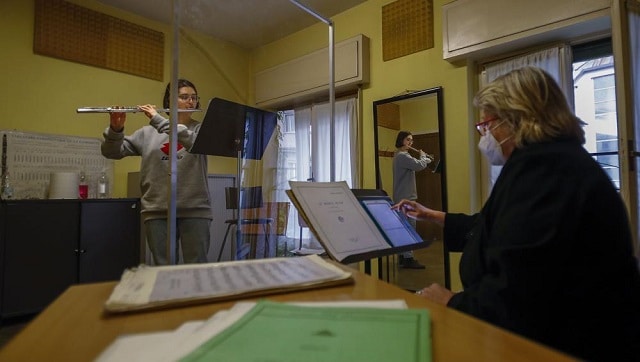 Linda Facchinetti plays her flute behind a transparent panel to curb the spread of COVID-19. Image via The Associated Press/Antonio Calanni