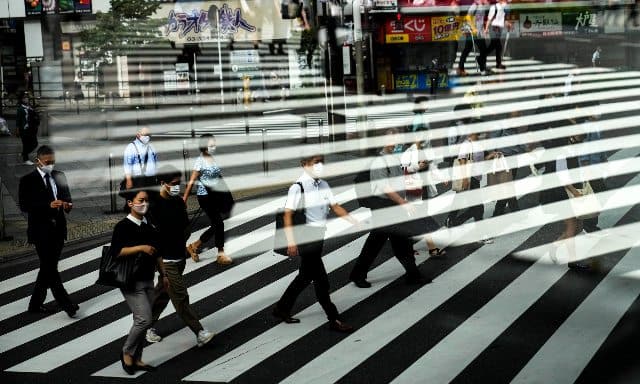 Commuters are reflected in a bus window as they cross the street. AP 