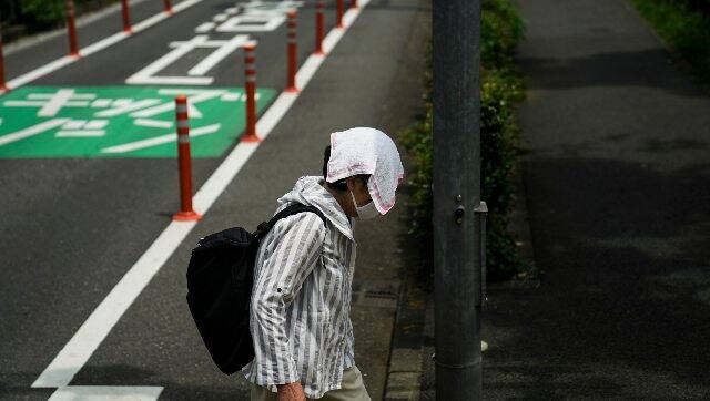 An elderly woman walks with a small towel over her head to shield from the sun. AP 