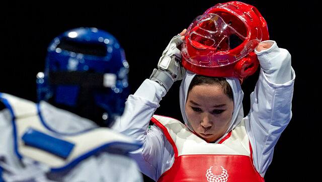 Zakia Khudadadi of Afghanistan (red) removes her helmet during her bout with Ziyodakhon Isakova of Uzbekistan (blue) in the women's K44 49kg round of 16 taekwondo at the Tokyo 2020 Paralympic Games on Thursday. Khudadadi is one to two Afghans participating in the Paralympics. She arrived in Tokyo days after the Paralympics opened, fleeing Kabul for Paris, and then on to Tokyo, after the Taliban took over the country. OIS via AP Photo