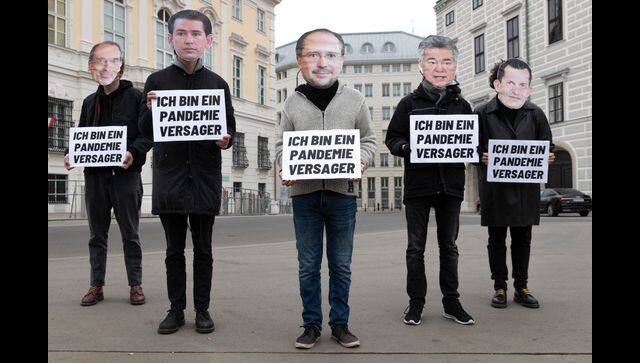 Protesters stand in front of the federal chancellery of Austria, wearing mask of the political leaders of Austria with a sign that says „ I am a pandemic failure