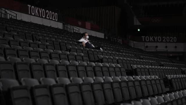 A man, wearing a protective face mask, sits inside an empty Ariake Arena, just before the start of a women's volleyball preliminary round pool A match between Japan and South Korea, at the 2020 Summer Olympics, Saturday, July 31, 2021, in Tokyo, Japan. AP
