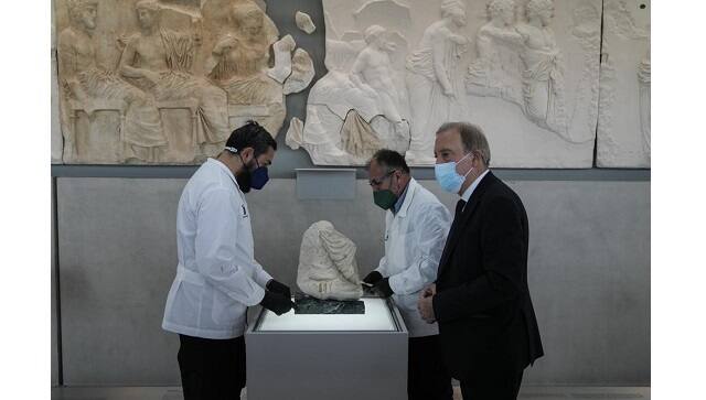 Acropolis Museum Director Nikolaos Stampolidis, right, and conservators stand next to a Parthenon fragment, on loan from the Antonino Salinas Regional Archaeological Museum of Palermo, at the Parthenon Gallery of the Acropolis Museum, in Athens, on Monday, Jan. 10, 2022 | (AP Photo/Thanassis Stavrakis)