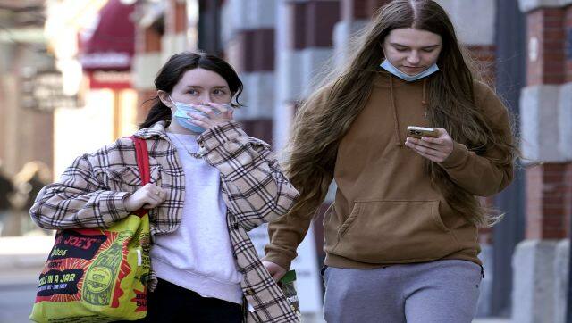 A passerby adjusts her mask, left, while walking on a sidewalk in the fashionable Newbury Street neighbourhood of Boston. Students and staff at public schools in Massachusetts will no longer be required to wear face coverings while indoors starting 28 February. AP