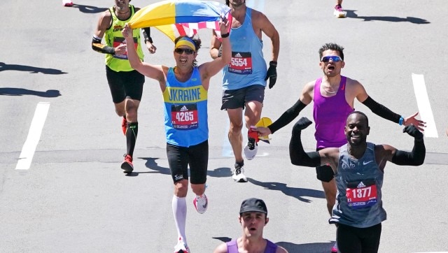 While dressed in a Ukraine shirt, a runner holds a Ukraine and American flag while approaching the finish line of the Boston Marathon, Monday, April 18, 2022, in Boston. (AP Photo/Charles Krupa)